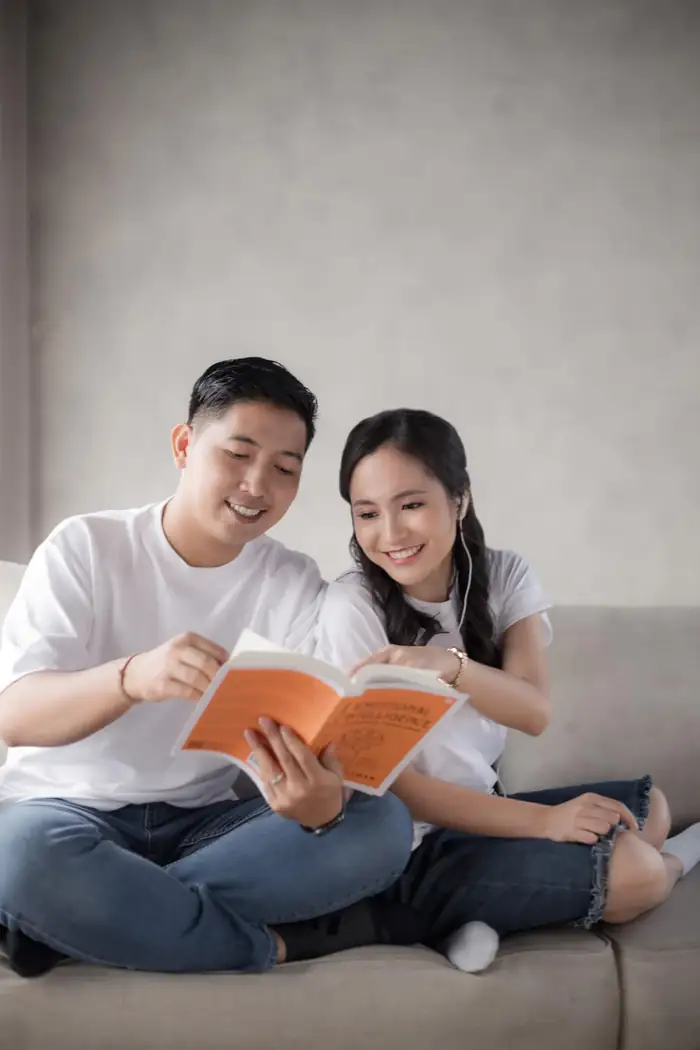 Kak Dianti dan pasangannya duduk di sofa sambil membaca buku bersampul oranye.