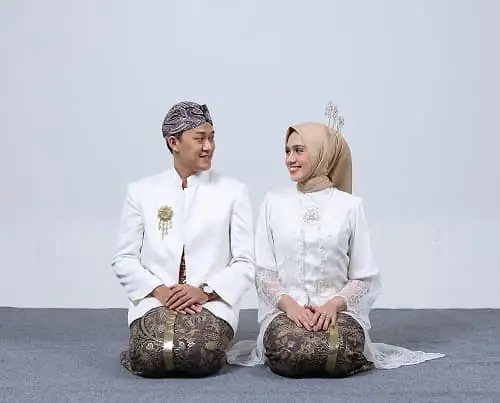 Kak Vinsky dan pasangannya berbaju adat putih dengan kain batik, duduk bersimpuh berdampingan.